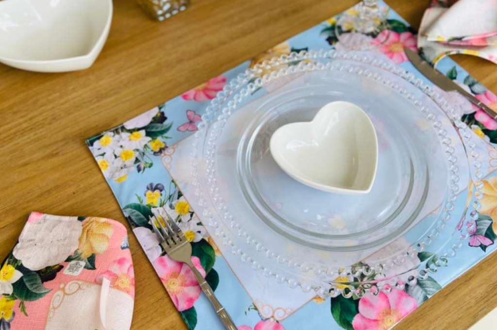 Imagem de mesa posta com toalha de mesa, pires e uma xícara em formato de coração.